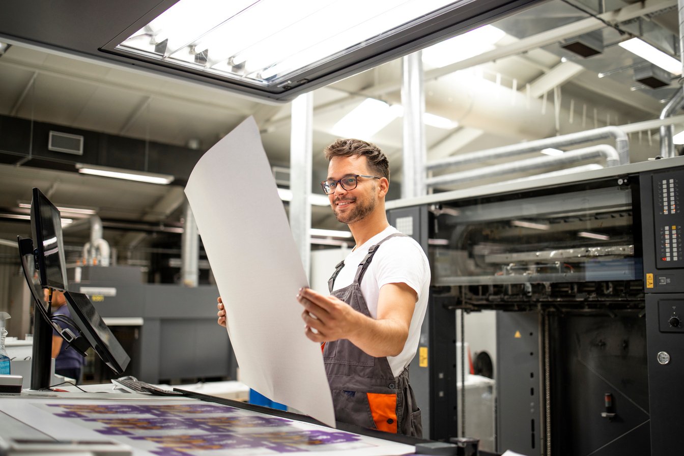 Print shop worker checking quality of imprint and controlling printing process.